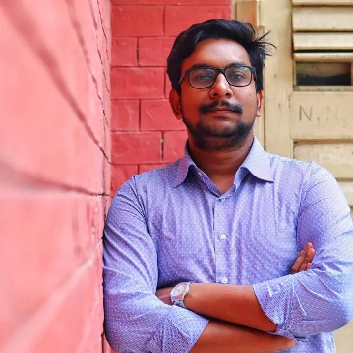 Shahad Mahmud, arms crossed, leaning against a red brick wall